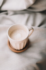 Cup of coffee with milk on beige plaid. Flat lay, top view still life morning breakfast. Comfort, cosiness and warmth concept. Photo in light pastel colors