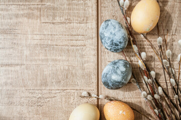 Beige and gray Easter eggs and pussy willow sprigs lie on a brown wooden surface. Copy Space