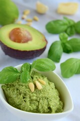 Basil avocado pesto sauce with main ingredients: fresh basil leaves, avocado, parmesan cheese, pine nuts, garlic and lime