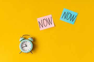 Alarm clock and a colored sticker with the inscription NOW on a yellow background