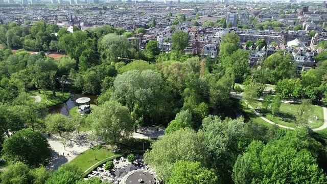 Aerial view of famous city park Vondelpark in Amsterdam, Netherland. Sunny day in summer or spring. People are resting and relaxing on green grass around lake.