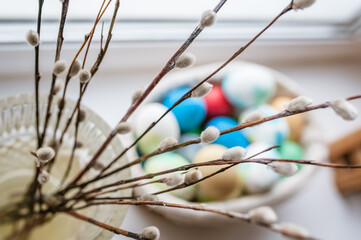 Willow branches in a vase, colored eggs in a basket on the windowsill and a festive Easter cake
