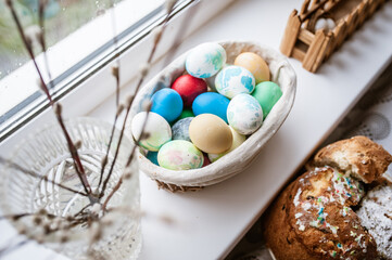 Willow branches in a vase, colored eggs in a basket on the windowsill and a festive Easter cake