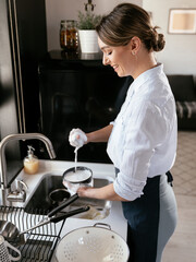 Beautiful young woman washing dishes at the kitchen sink. Happy smiling woman in the kitchen