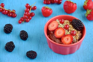Chocolate oatmeal porridge with strawberry, blackberry, red currant, hemp seeds and flax seeds. Blueberry background
