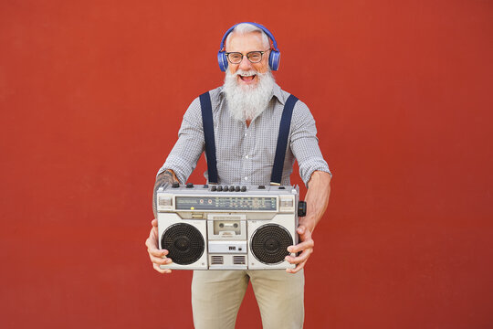 Happy senior man having fun listening to music with wireless headphones and vintage boombox outdoor