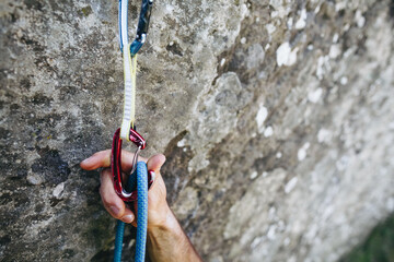 Close up of rock climber hand clipping rope in a quick draw caribener on a cliff face