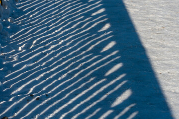 A shadow in the snow from an old rusty fence. Straight lines in the snow. Minimalist photography.