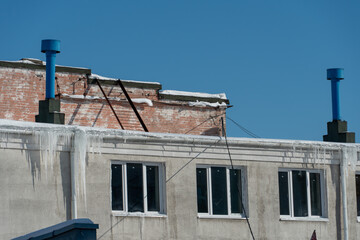The roofs of the buildings are covered with snow and ice after a big snowfall. Huge icicles hang from the facades of buildings. The fall of icicles carries a danger to people's lives.