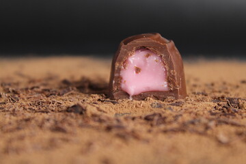 Chocolate's day enclosure chocolate candy with stuffing rests on cocoa on a grey black background with a place to text a copy of the sweet chocolate brown background