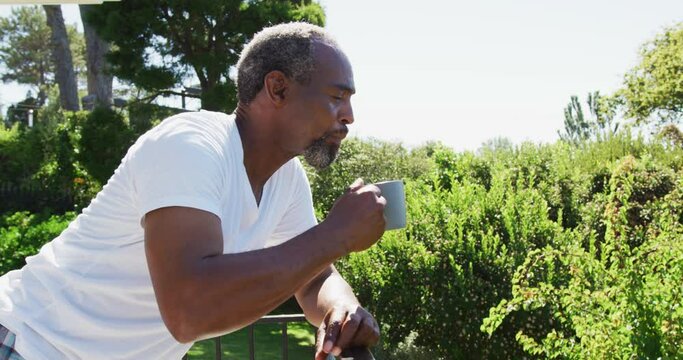 Senior african american man standing on balcony drinking coffee on sunny day