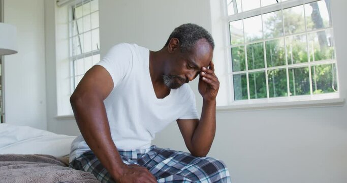 Senior african american man with headache sitting on bed holding head
