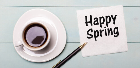 On a light blue wooden tray, there is a white cup of coffee, a handle and a napkin that says HAPPY SPRING