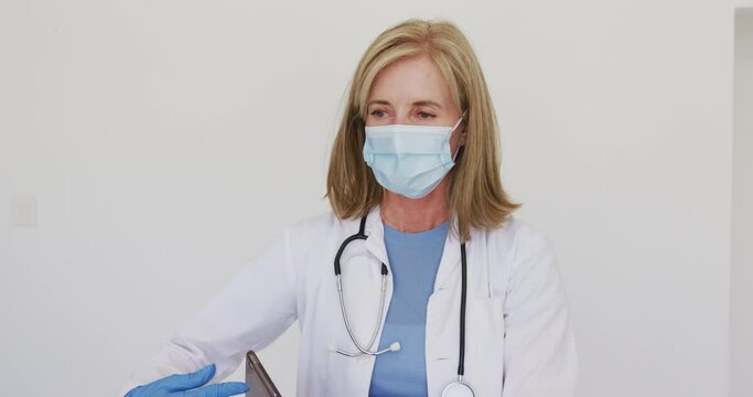 Portrait of caucasian senior female doctor wearing surgical gloves and face mask using tablet comput