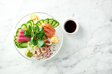 Classic Japanese sashimi set of raw salmon, eel and tuna with lime, cucumber on plate on a marble background. Close up, selective focus