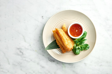 Asian street food - Deep-fried spring roll in rice paper served in a beige plate with spicy chili sauce on a marble background. Restaurant food.