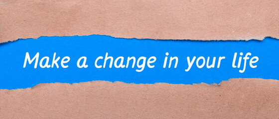 A strip of blue paper with the words MAKE A CHANGE IN YOUR LIFE between the brown paper. View from above