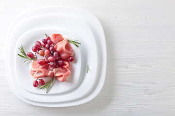 Prosciutto with rosemary and grapes on a white plate.