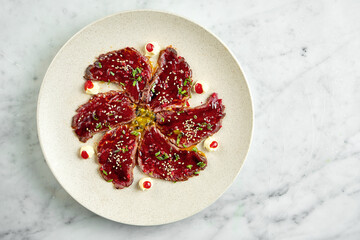Japanese classic dish - tataki beef with unagi sauce, hot pepper, served in a beige plate on a marble background. Restaurant food