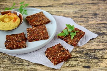 Homemade seed crackers made from bell pepper, sun dried tomato, sunflower seed, sesame seed, hemp seed and flax seeds. Served with hummus dip