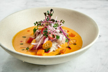 Peruvian cuisine dish - seabass ceviche with hot peppers, onions and yellow sauce, served in a white plate on a marble background. Restaurant seafood.