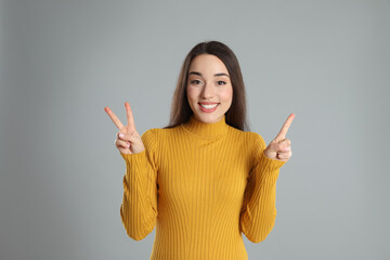 Woman in yellow turtleneck sweater showing number three with her hands on grey background