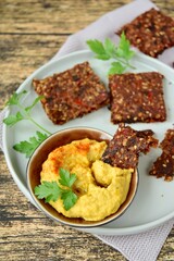 Seed crackers made from bell pepper, sun dried tomato, sunflower seed, sesame seed, hemp seed and flax seeds. Garnish with parsley, serve with hummus