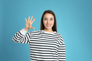 Woman showing number five with her hand on light blue background