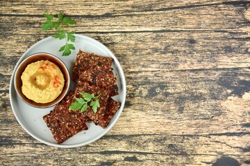 Homemade seed crackers made from bell pepper, sun dried tomato, sunflower seed, sesame seed, hemp seed and flax seeds. Served with hummus dip
