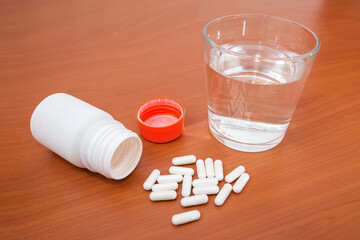 Glass of water and pills on a wooden table