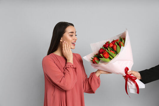 Happy woman receiving red tulip bouquet from man on light grey background. 8th of March celebration