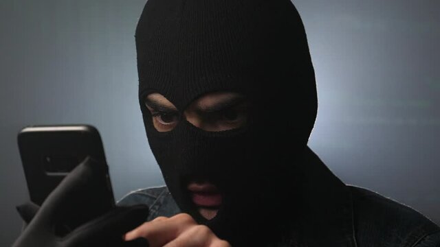Hacker with a cell phone and a facemask hacking the system