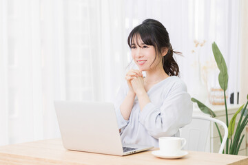 部屋でノートパソコンを使いながらお願いのジェスチャーをする若い女性