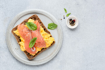Scrambled eggs and smoked salmon on rye bread toast. Top view. Healthy breakfast or lunch sandwich. Grey concrete background, copy space