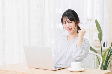 部屋でノートパソコンを使いながらガッツポーズをする若い女性