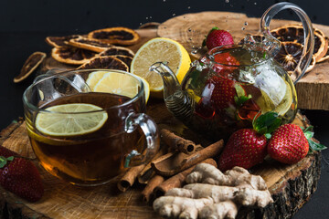 Fototapeta na wymiar Glass teapot. Still life with hot tea with lemon and strawberries. Wooden stand. Splash.