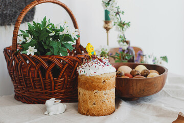 Obraz na płótnie Canvas Homemade Easter bread, modern eggs, basket, bunny and blooming spring flowers on rustic table