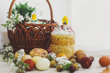 Homemade Easter bread, modern eggs, basket, bunny and blooming spring flowers on rustic table