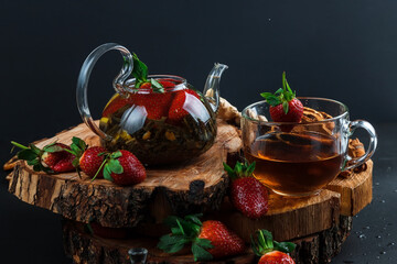 Fototapeta na wymiar Hot tea with lemon and strawberries. Glass teapot. Wooden stand. Splash.