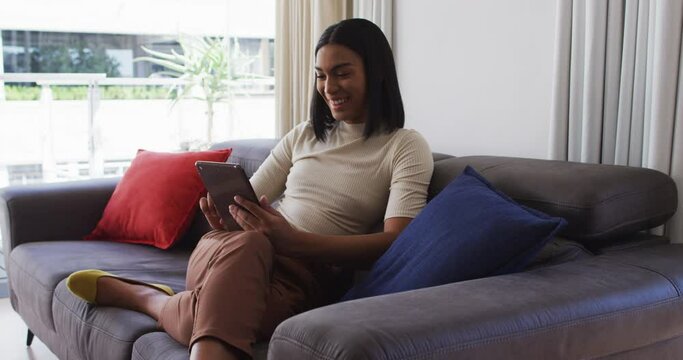 Mixed race gender fluid person sitting on couch and using tablet at home