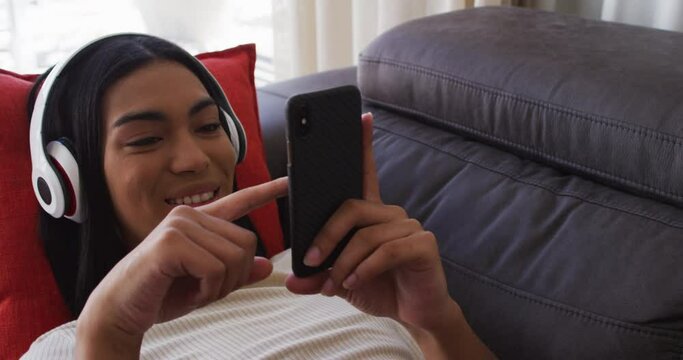 Mixed race gender fluid person sitting on couch using smartphone and listening to music at home