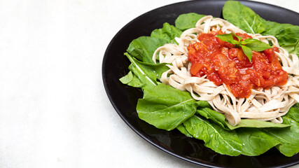wholemeal pasta pasta with green leaves of arugula, red sauce and balsamic vinegar on black plate and white marble background