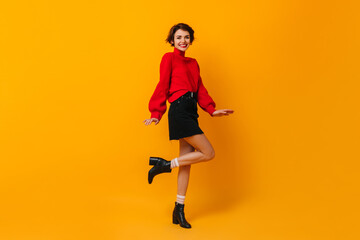 Fototapeta na wymiar Positive girl with short hair dancing on yellow background. Studio shot of happy slim woman in red sweater.