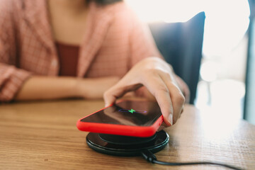 Fototapeta premium Charging mobile phone battery with wireless charging device in the table. Smartphone charging on a charging pad. Mobile phone near wireless charger Modern lifestyle concept.