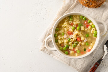 Tasty soup with ditalini pasta, peas, tomatoes, ham on white table. Close up. Copy space.