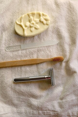 Sustainable toiletries on linen cloth: reusable metal safety razor, wooden toothbrush, glass nail file and soap bar. Top view.