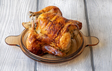 Homemade tasty rotisserie chicken on white wooden surface.
