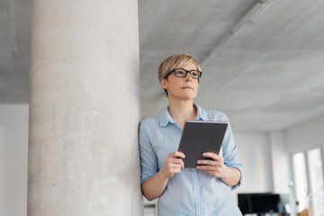 Thoughtful woman standing holding a tablet-pc