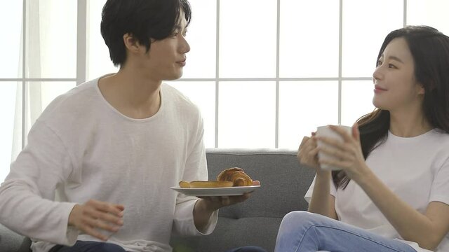 Loving couple sitting on sofa at home. Man and woman relaxing on couch with smartphone in living room.