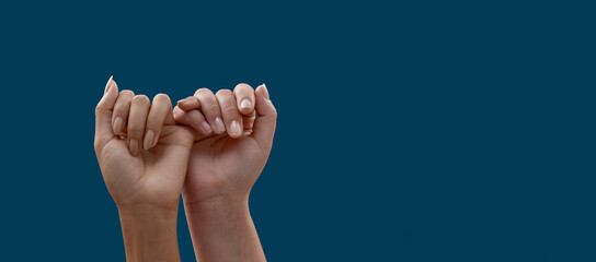 Two hands hook each other little finger pinkie as a symbol of promise or pardon isolated on blue background